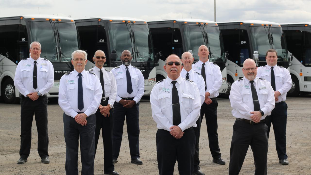 Nine NW Navigator drivers in white uniform shirts and ties, standing in front of a line of coaches