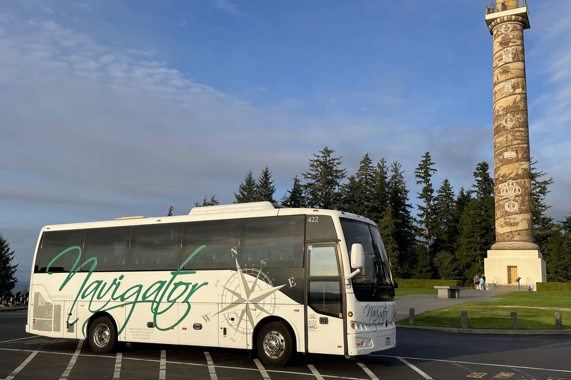 An NW Navigator coach parked near a stone monument in evening light