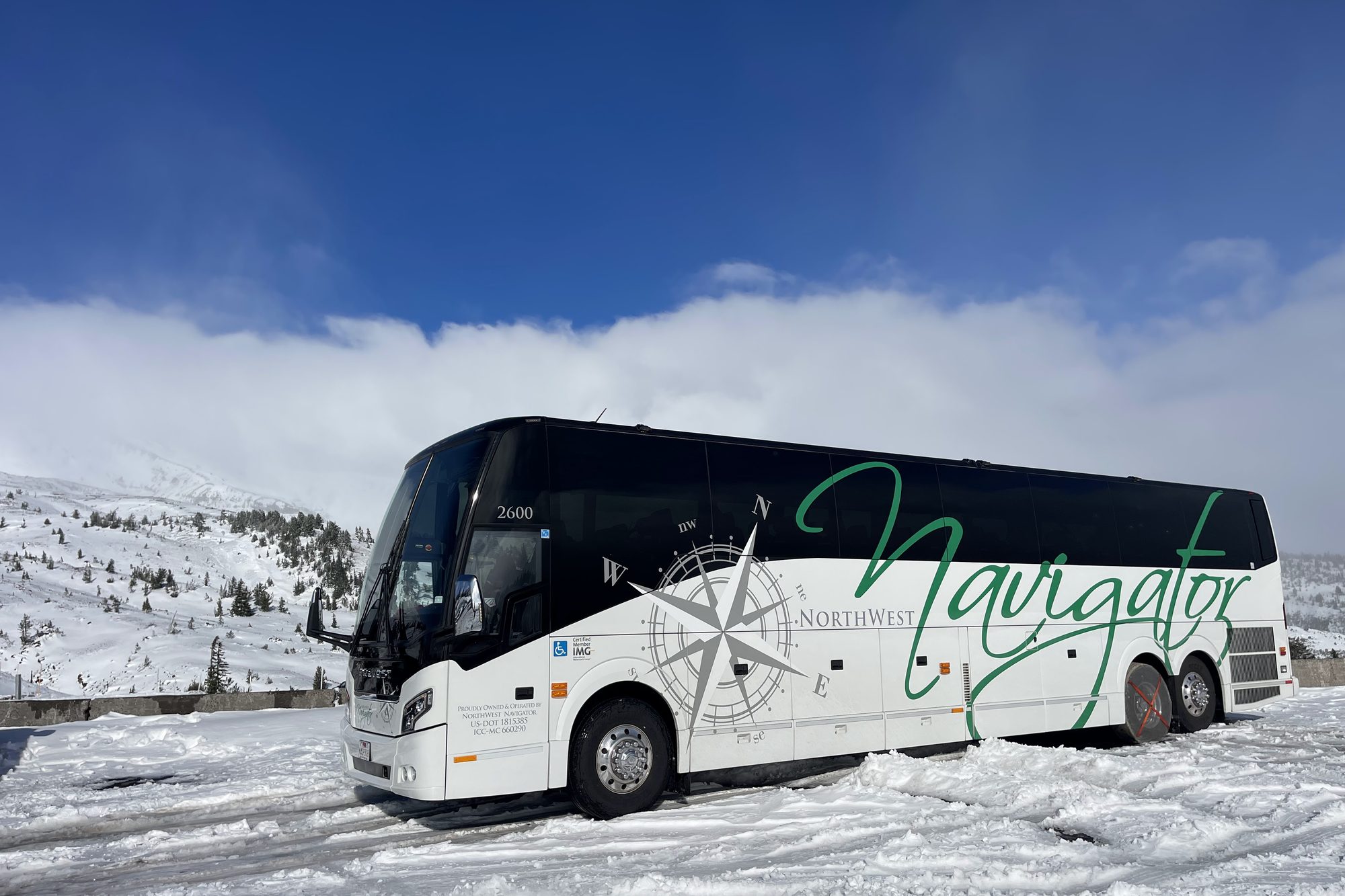 An NW Navigator coach parked in snow below a mountain ridge